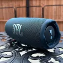 JBL Charge 5 JBLCHARGE5 blue speaker resting on an ornate metal patio table outdoors - CairoVolt