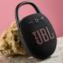 سماعة JBL Clip 5 سوداء مستندة على صخرة أمام خلفية وردية - كايرو فولت